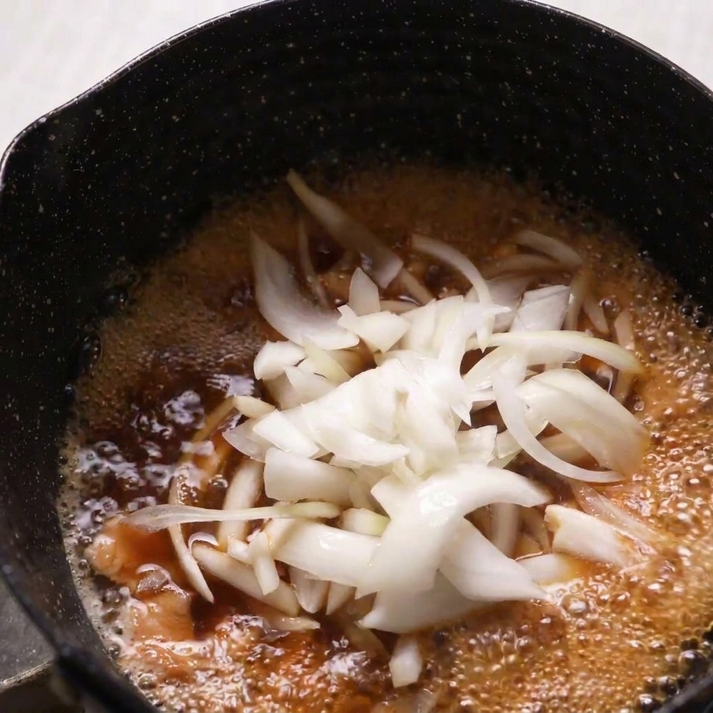 Fines lamelles doignons crus ajoutées à une poêle de poulet et de bouillon dashi frémissant.