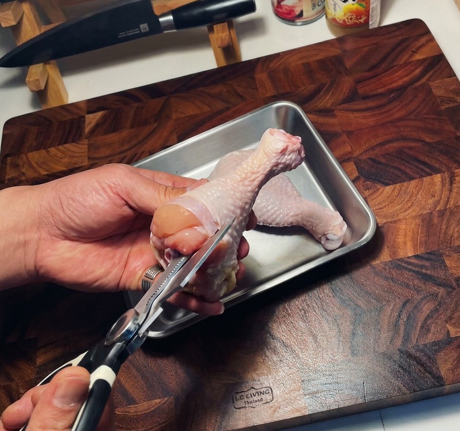 Utilisation de ciseaux de cuisine pour retirer los dun haut de cuisse de poulet cru au-dessus dun plateau.