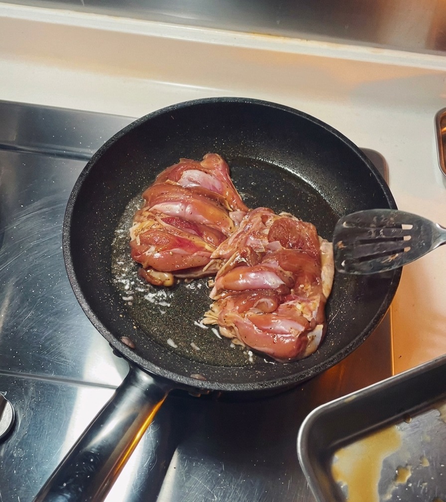 Deux hauts de cuisses de poulet assaisonnés grillant côté peau dans une poêle noire jusquà ce que la peau soit dorée.
