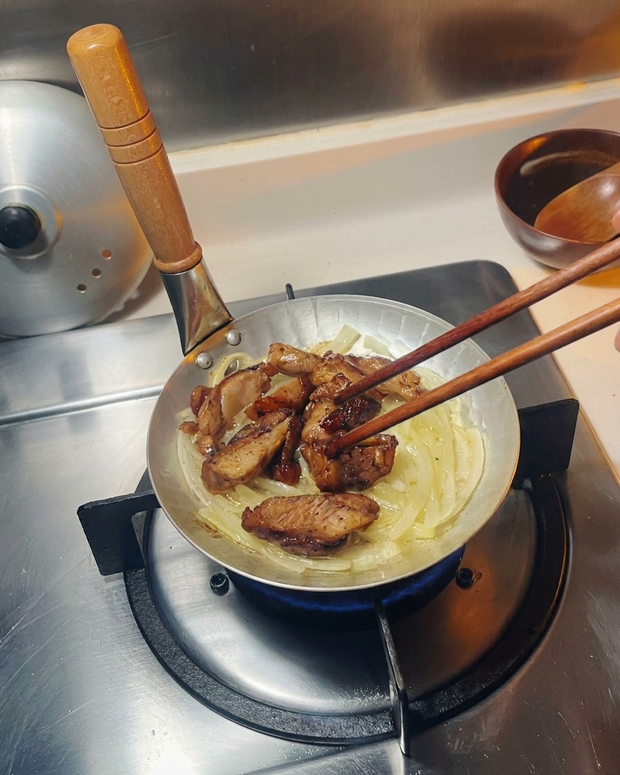Morceaux de poulet grillé placés sur un lit doignons translucides dans une petite poêle argentée.