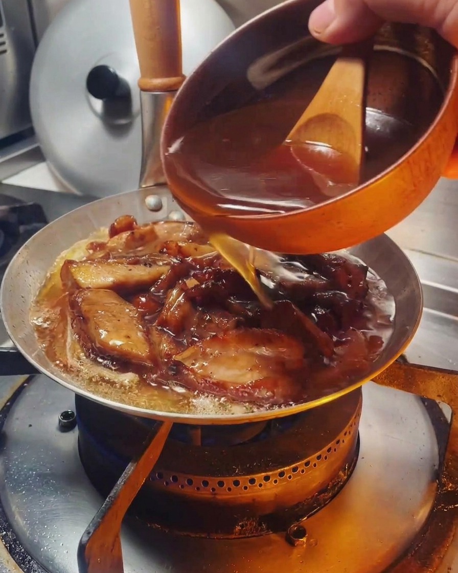 Sauce brune versée dun bol à manche en bois dans une poêle contenant le poulet et les oignons.