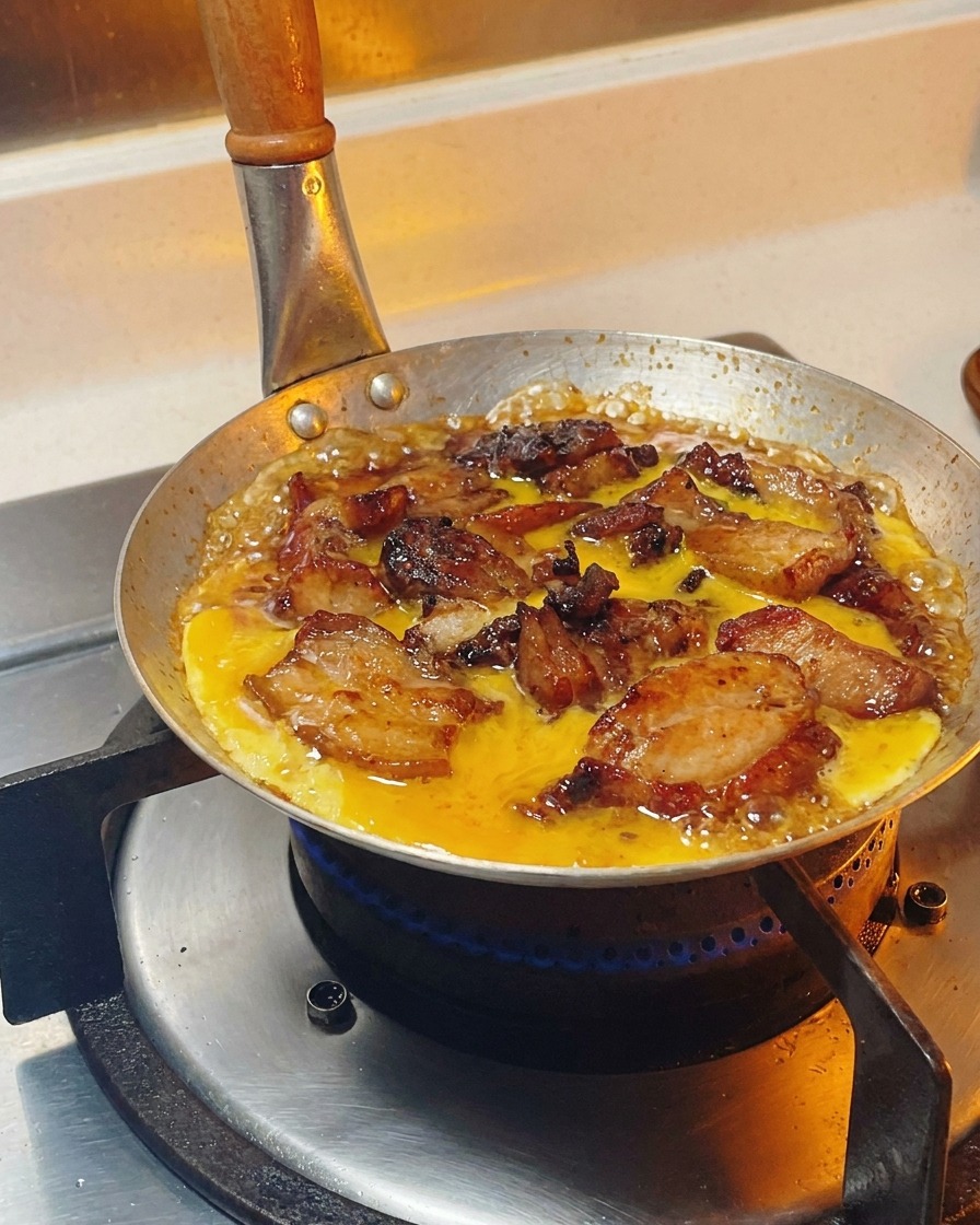 Mélange dœufs battus versé en cercle sur le poulet et les oignons mijotant dans la sauce.