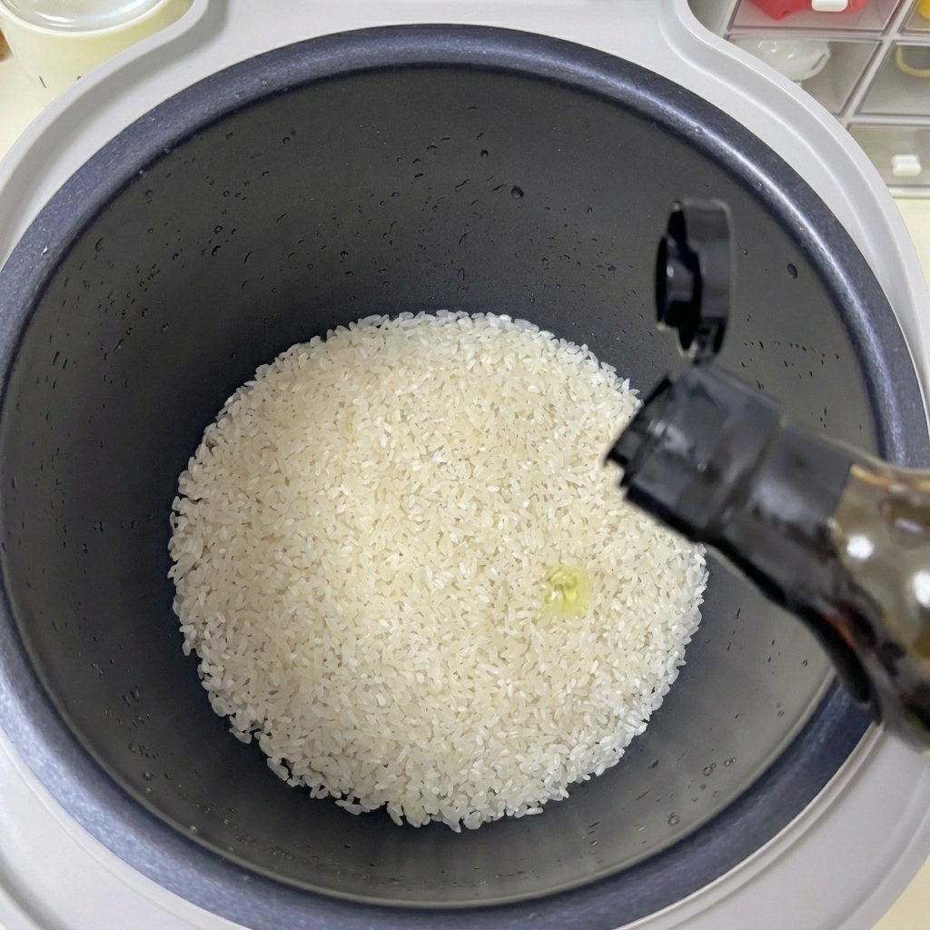 Une main versant un filet dhuile claire depuis une bouteille sombre dans un cuiseur à riz rempli de riz blanc.