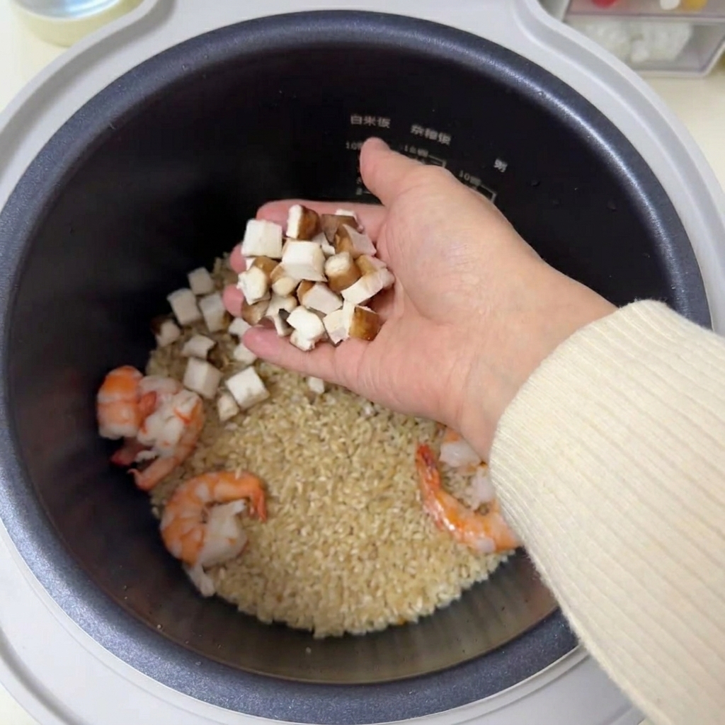 Des morceaux de champignons shiitakés bruns tenus dans une main au-dessus dun cuiseur à riz contenant du riz et des crevettes.