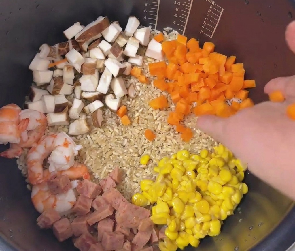 Une disposition colorée de carottes en dés, maïs, jambon, champignons et crevettes superposés sur le riz dans une cuve.