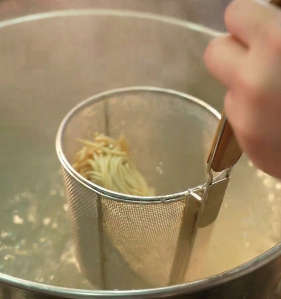 Une passoire à nouilles contenant des ramen plongée dans une grande casserole deau bouillante.