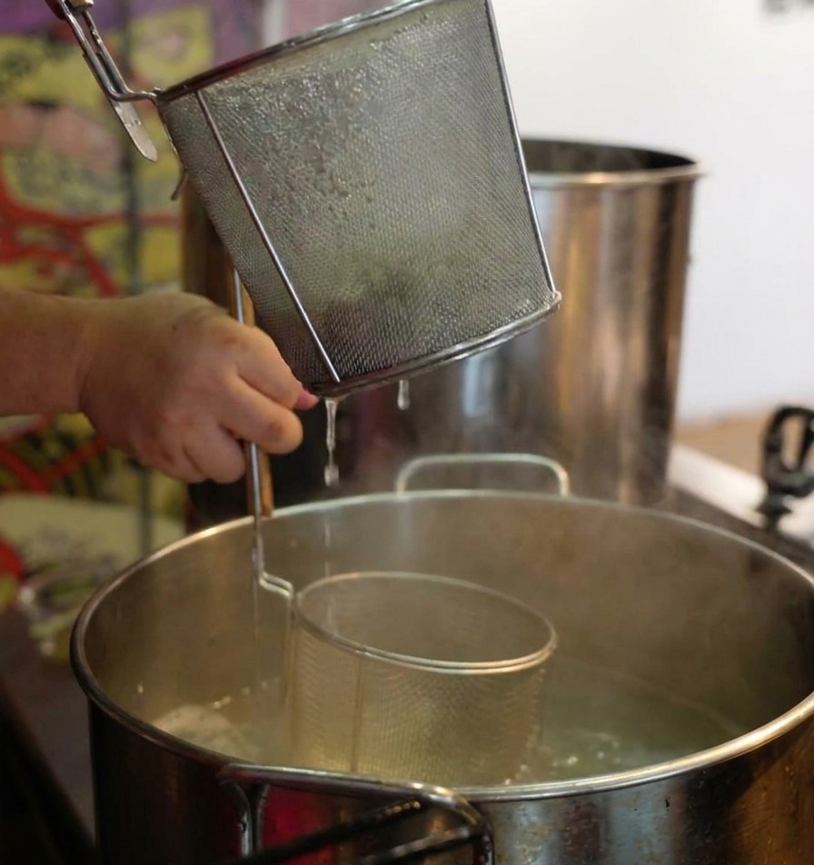 Des mains secouant une passoire à nouilles au-dessus dune casserole de vapeur pour égoutter les ramen cuits.