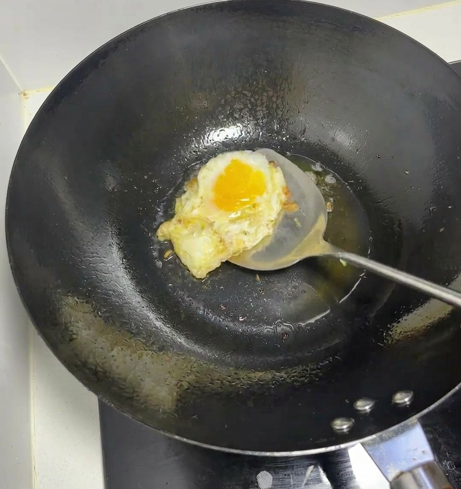 Un œuf en train de frire dans un wok chaud avec une spatule métallique.