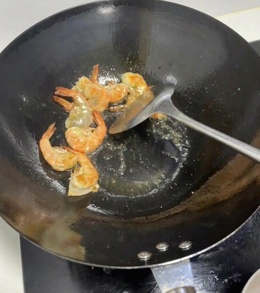 Des crevettes entières devenant roses dans un wok brûlant.
