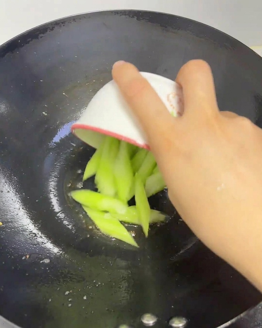 Tranches de luffa vert frais versées dans un wok chaud.