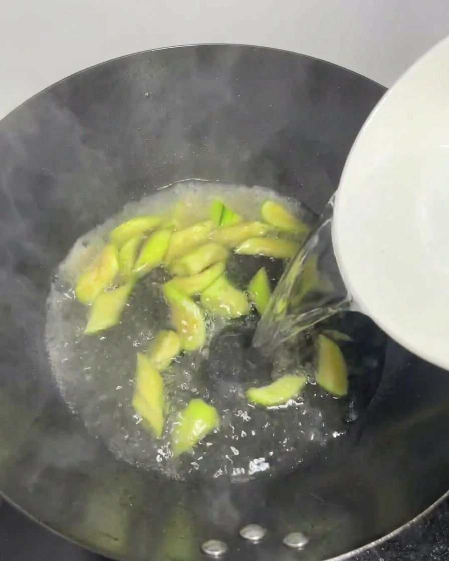 De leau claire versée dans un wok bouillonnant avec des tranches de luffa.