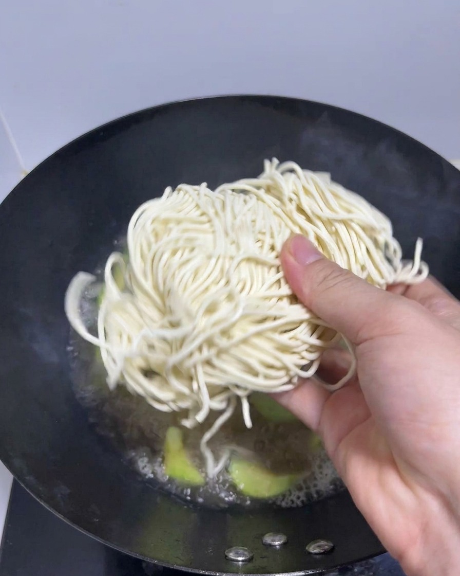 Une main déposant des nouilles ramen fraîches dans le bouillon bouillant.