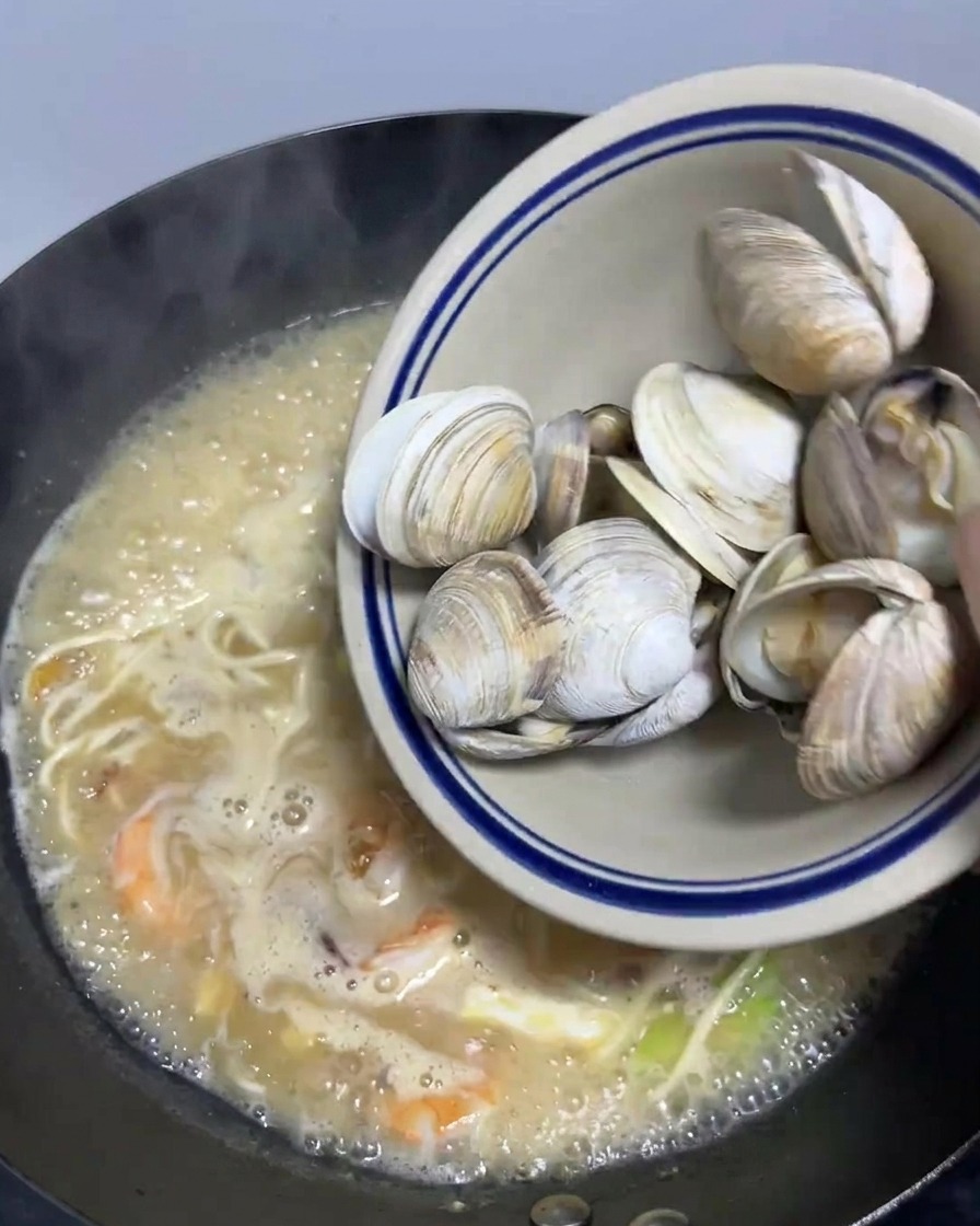Un bol de palourdes blanchies versé dans le wok de ramen.