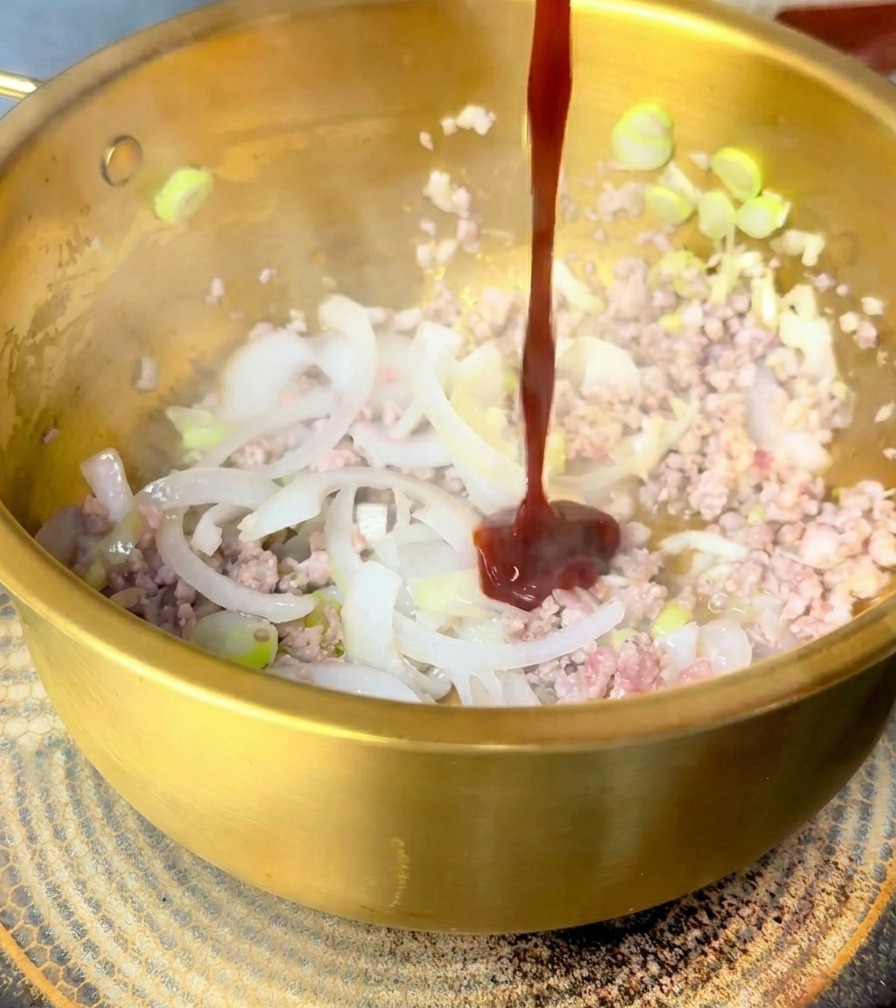 Un filet épais de sauce rouge foncé versé sur le porc et les oignons sautés.