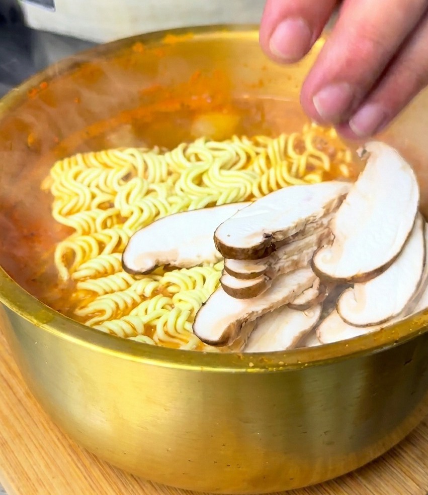 Une main disposant des tranches de shiitakés sur les nouilles immergées dans la soupe rouge.