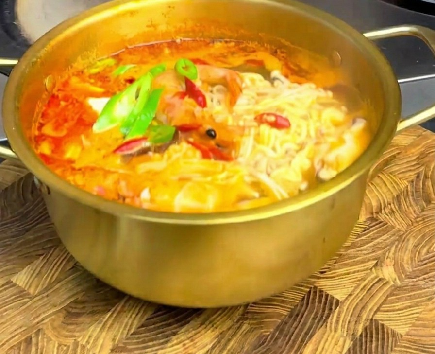 Ramen épicé aux fruits de mer garni de rondelles de piments verts et rouges sur une planche en bois.