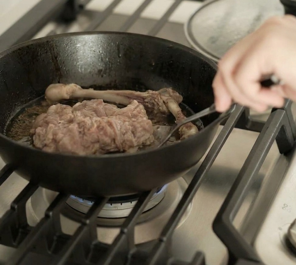La cuisse de canard retournée dans la poêle, montrant une peau parfaitement dorée et croustillante.