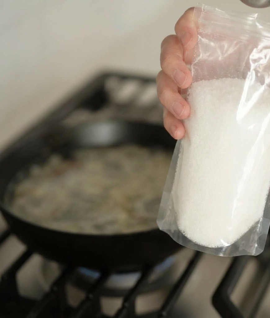 Une main tenant un sachet et versant une poudre dassaisonnement blanche dans un bouillon frémissant.