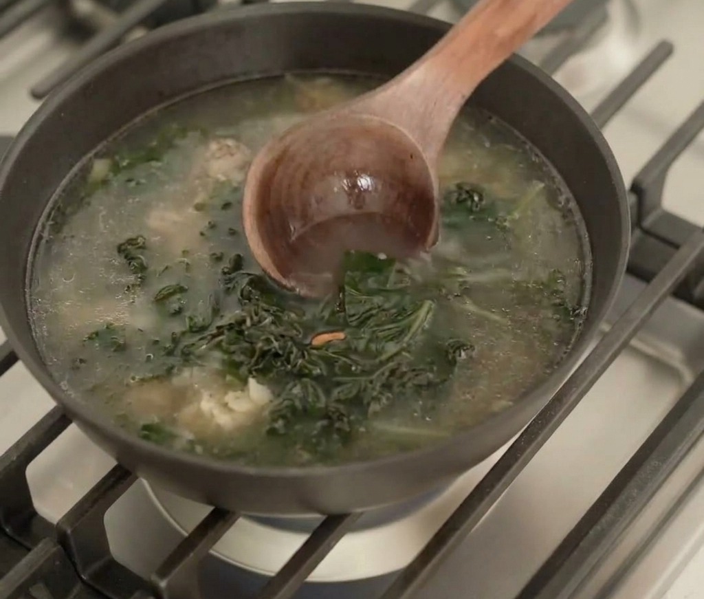 Une louche en bois remuant un bouillon frémissant avec des morceaux dalgues réhydratées dans une poêle.