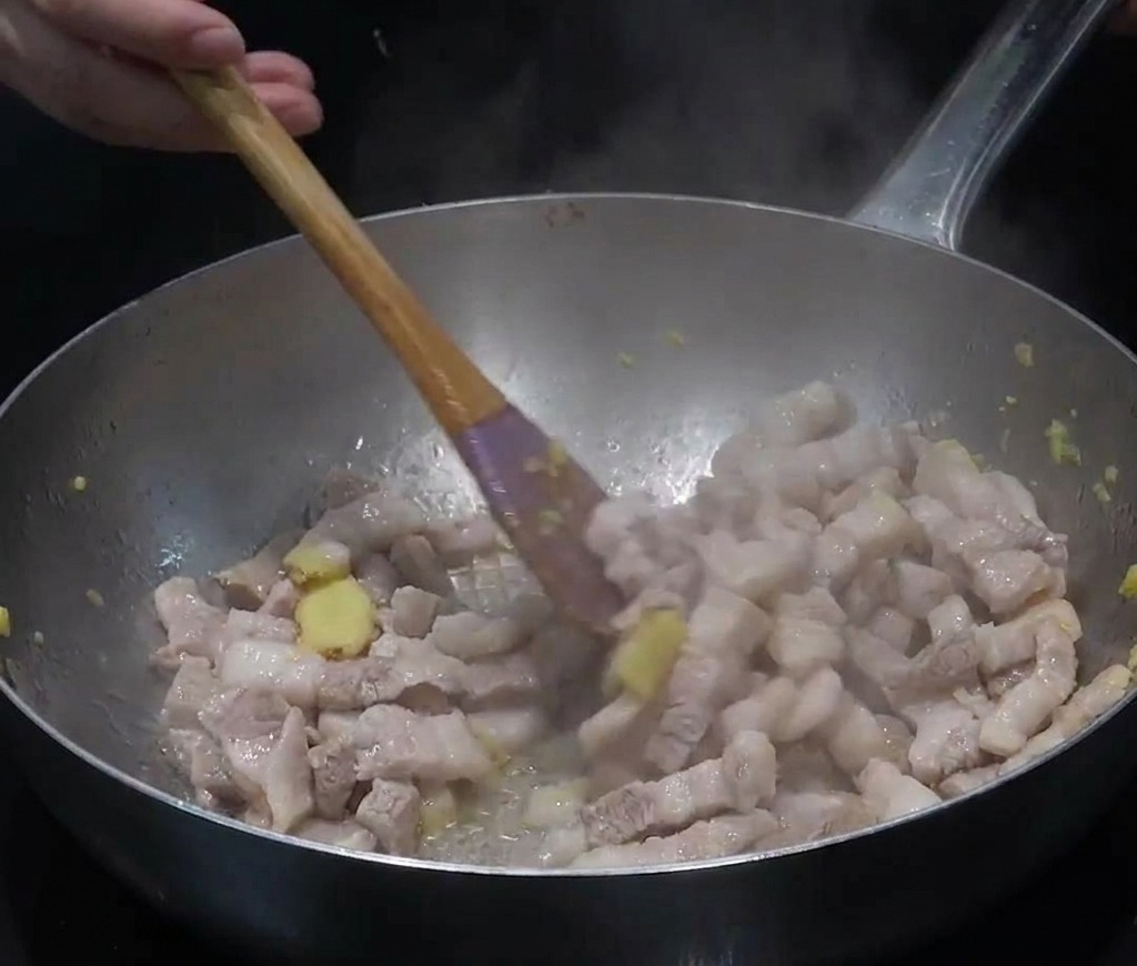 Tranches de poitrine de porc et gingembre haché sautés dans une grande poêle en inox avec de la vapeur.