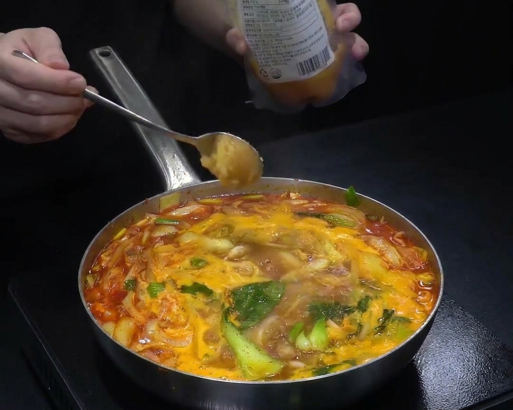 Une cuillerée dail haché ajoutée à une large poêle de soupe rouge bouillante remplie de chou et doignons.