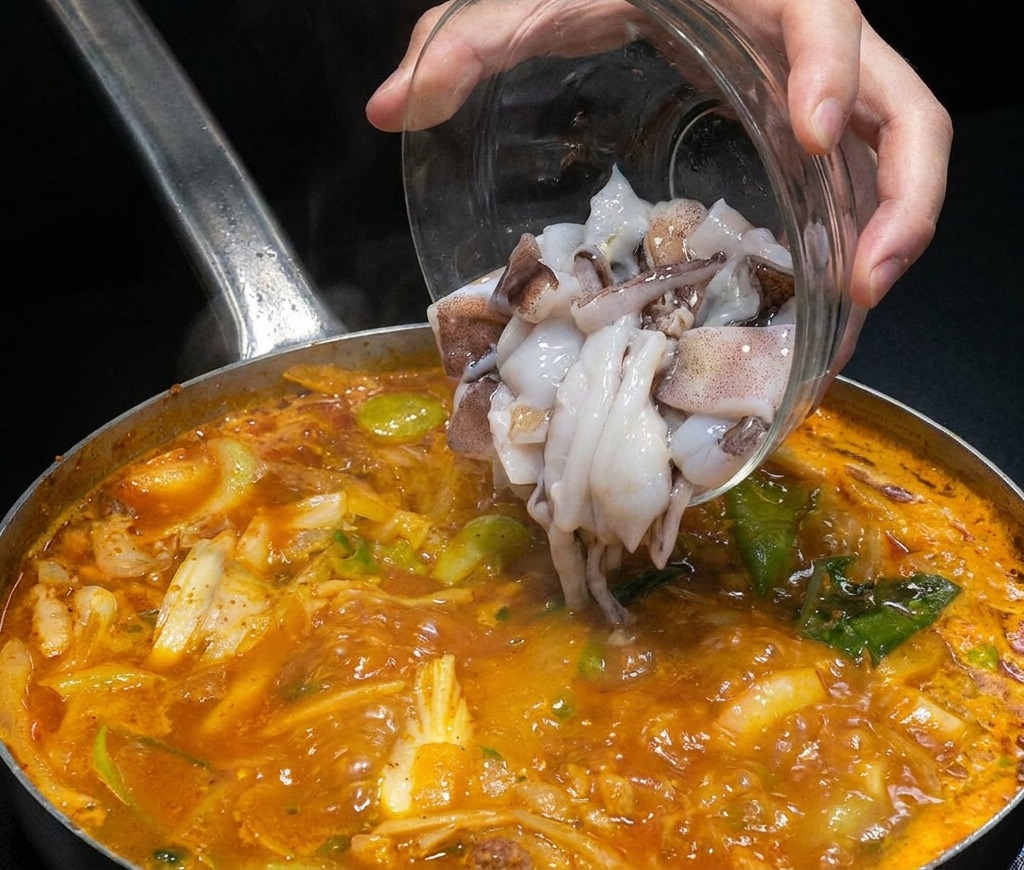 Morceaux de calmars crus versés dun bol en verre dans une marmite de bouillon de fruits de mer fumant.