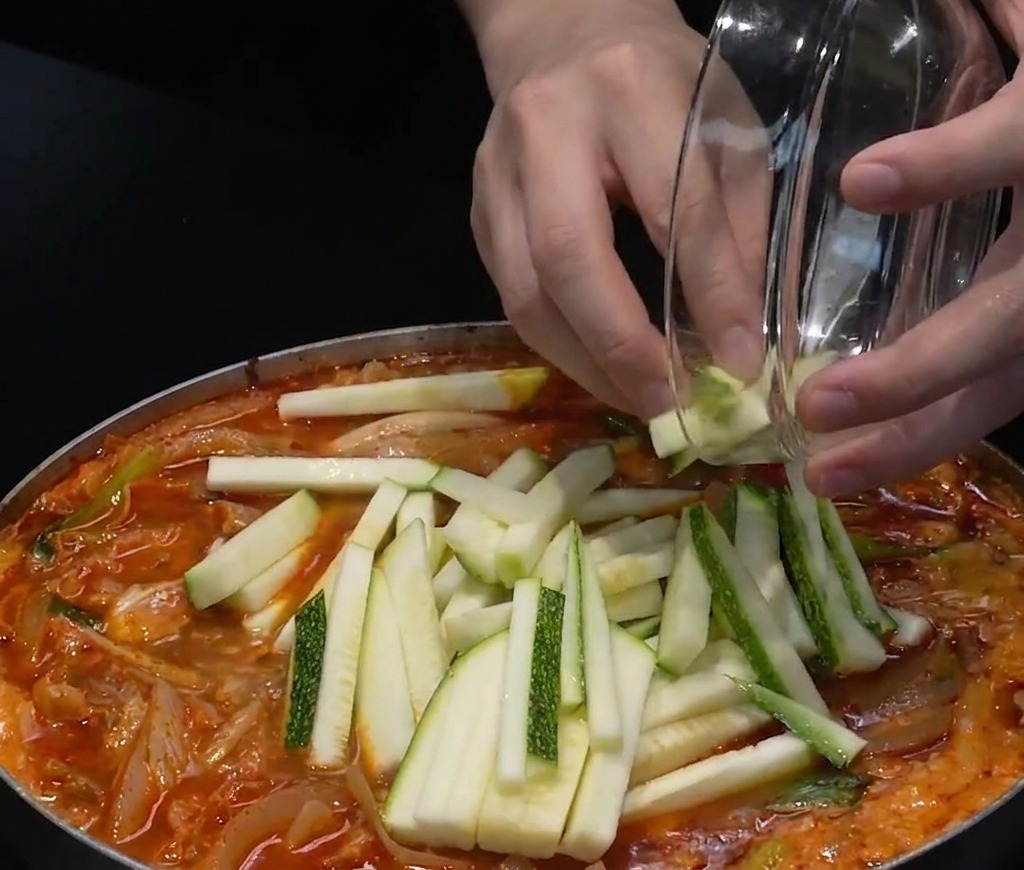 Courgettes tranchées et piments verts hachés ajoutés sur le dessus dune marmite de soupe rouge.