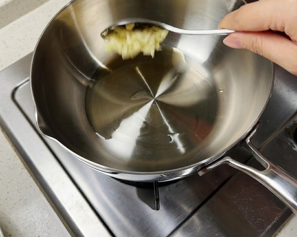 Une cuillerée dail haché ajoutée dans une marmite contenant de lhuile chaude et des oignons verts hachés.