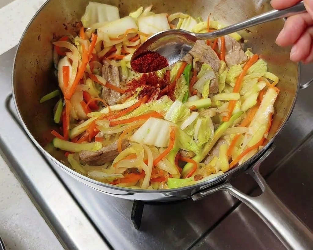De la poudre de piment coréen dun rouge vif saupoudrée sur les légumes sautés dans la marmite.