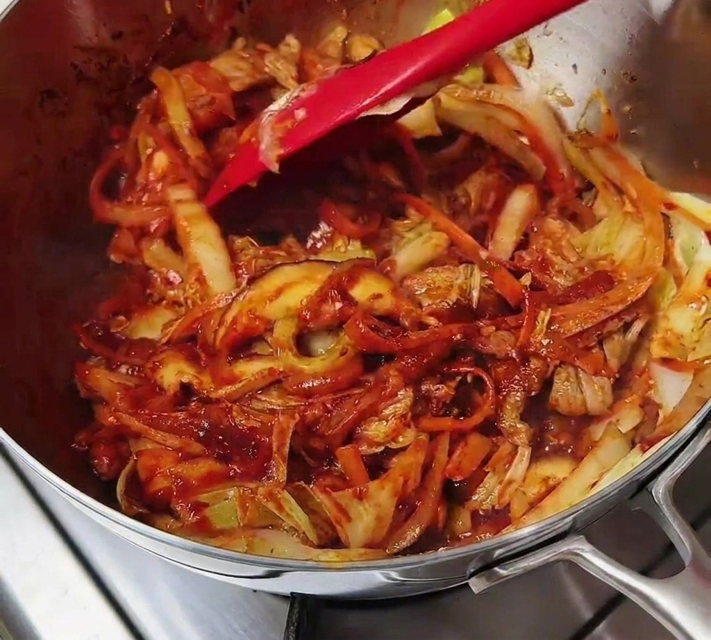 Une spatule rouge remuant un mélange de viande et de légumes enrobés dun riche assaisonnement rouge pimenté.