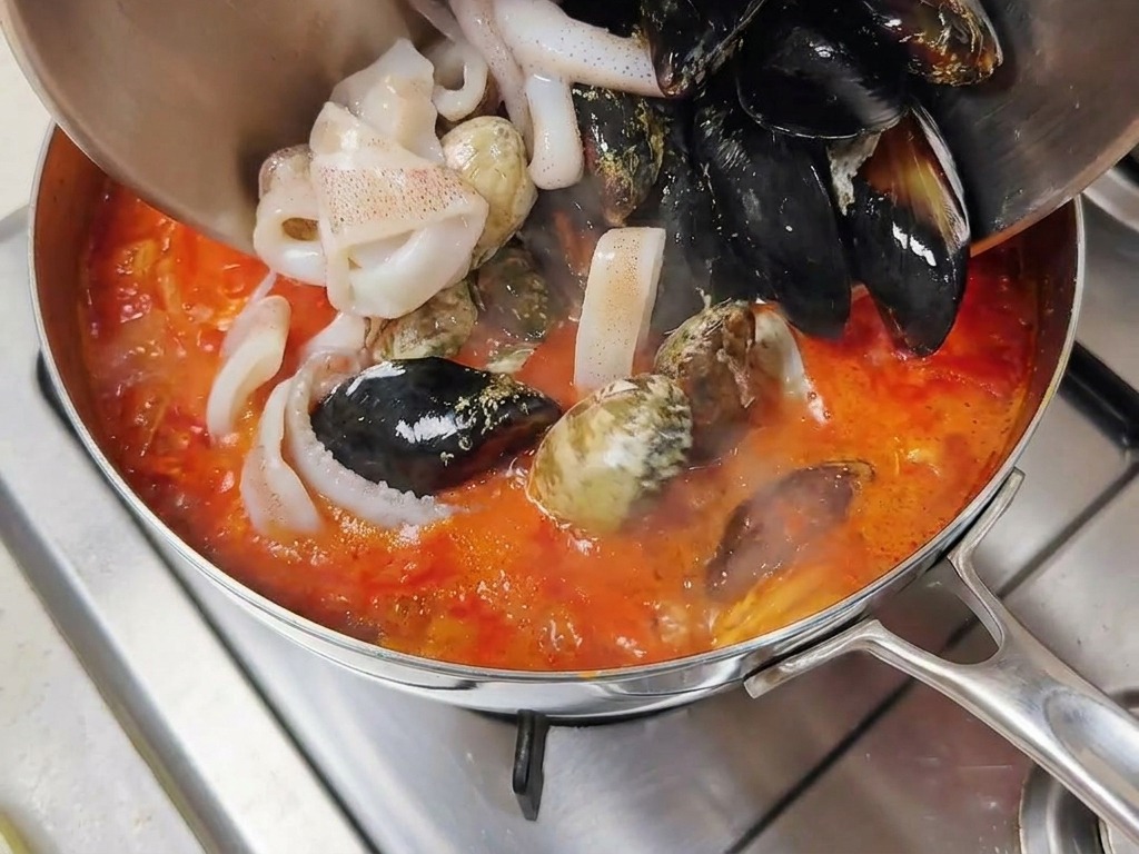 Des fruits de mer frais, dont des moules en coquilles noires et des anneaux de calamar, versés dans un bouillon rouge bouillonnant.