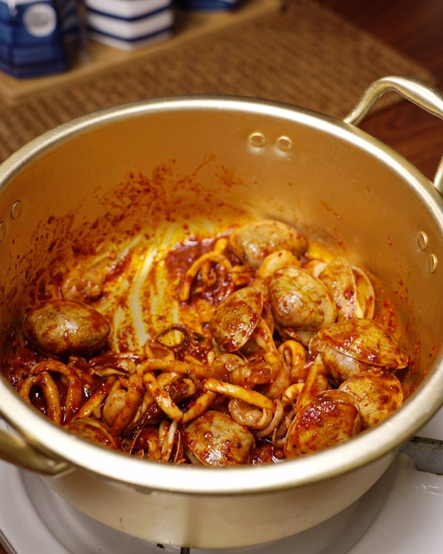 Calmars, crevettes et palourdes enrobés de piment rouge éclatant et dépices sautant dans une marmite dorée.