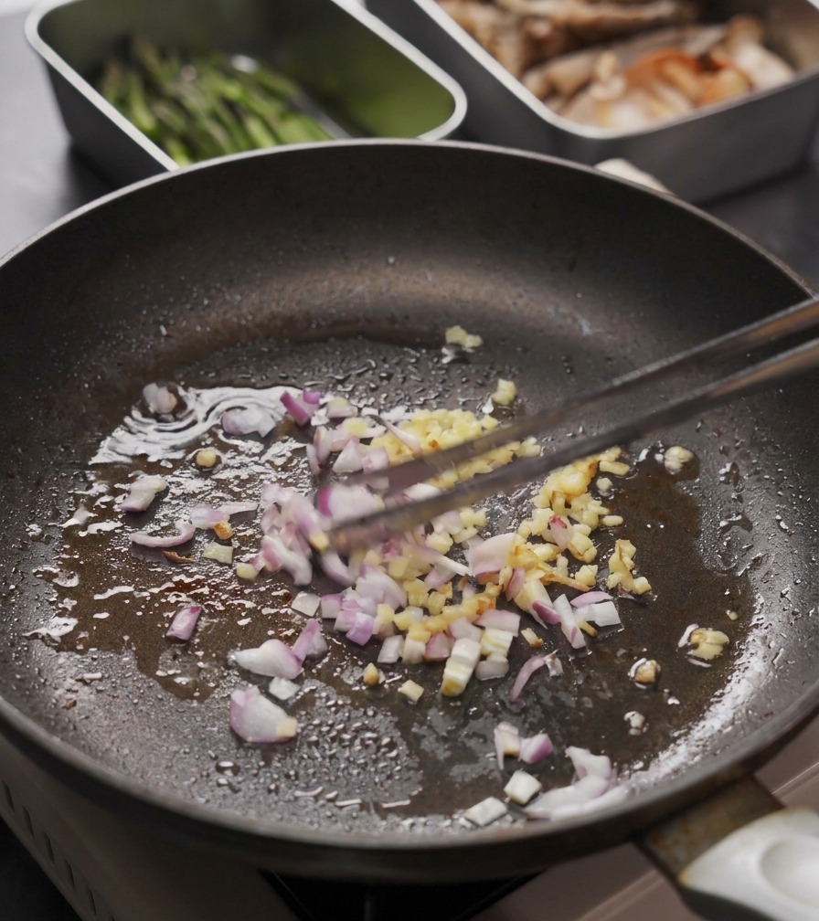 Gingembre haché et oignons rouges remués dans une poêle avec une pince de cuisine.