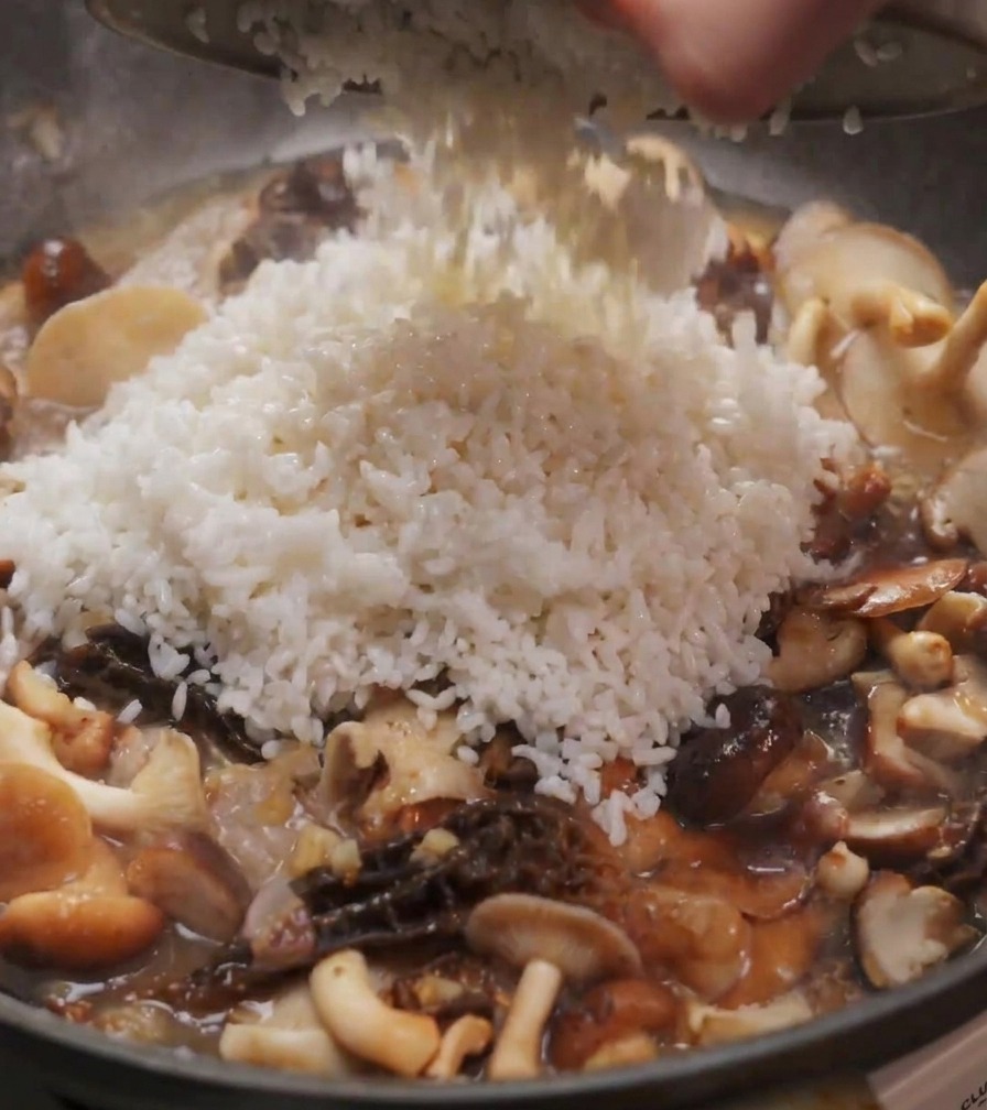Une portion de riz blanc versée dun bol dans une poêle remplie de shiitakes et de morilles sautés.