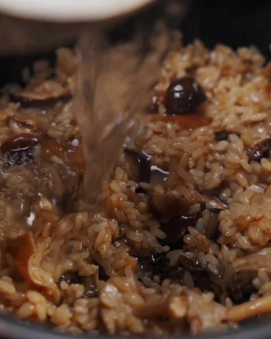 Eau versée dans un récipient contenant un mélange assaisonné de riz et de champignons.