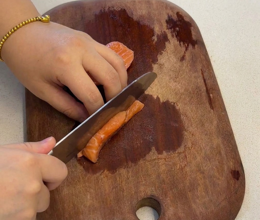 Une main utilisant un couteau pour couper un filet de saumon frais en petits cubes uniformes sur une planche en bois.