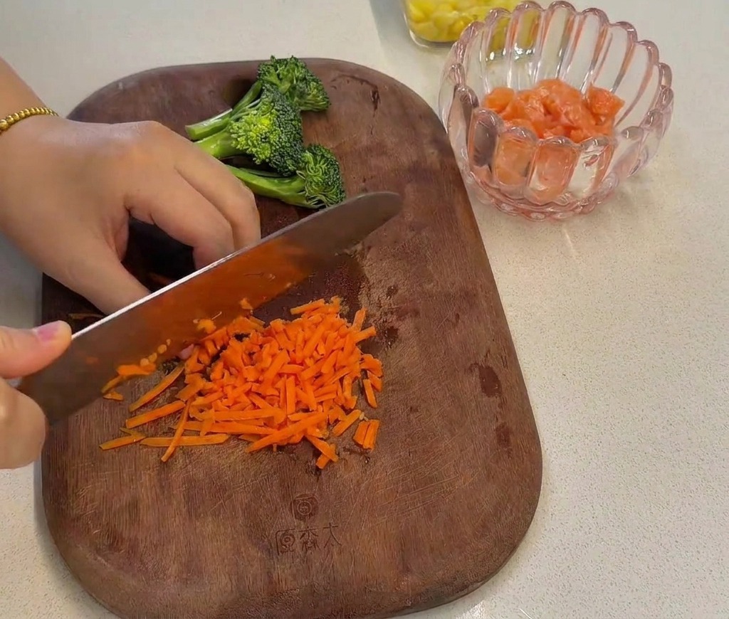 Carottes râpées hachées finement avec un couteau de chef sur une planche en bois.
