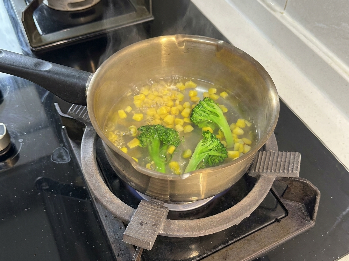 Une casserole deau bouillante contenant des fleurettes de brocoli et des grains de maïs.