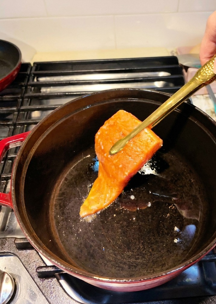 Filets de saumon marinés déposés dans une cocotte en fonte chaude à laide dune pince de cuisine.