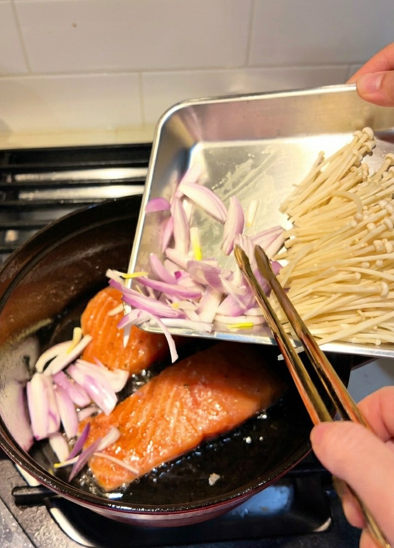 Échalotes émincées ajoutées dans une cocotte où les filets de saumon sont en train de saisir.