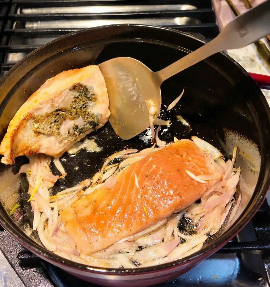 Une spatule métallique retournant un filet de saumon dans une cocotte, montrant une surface dorée.