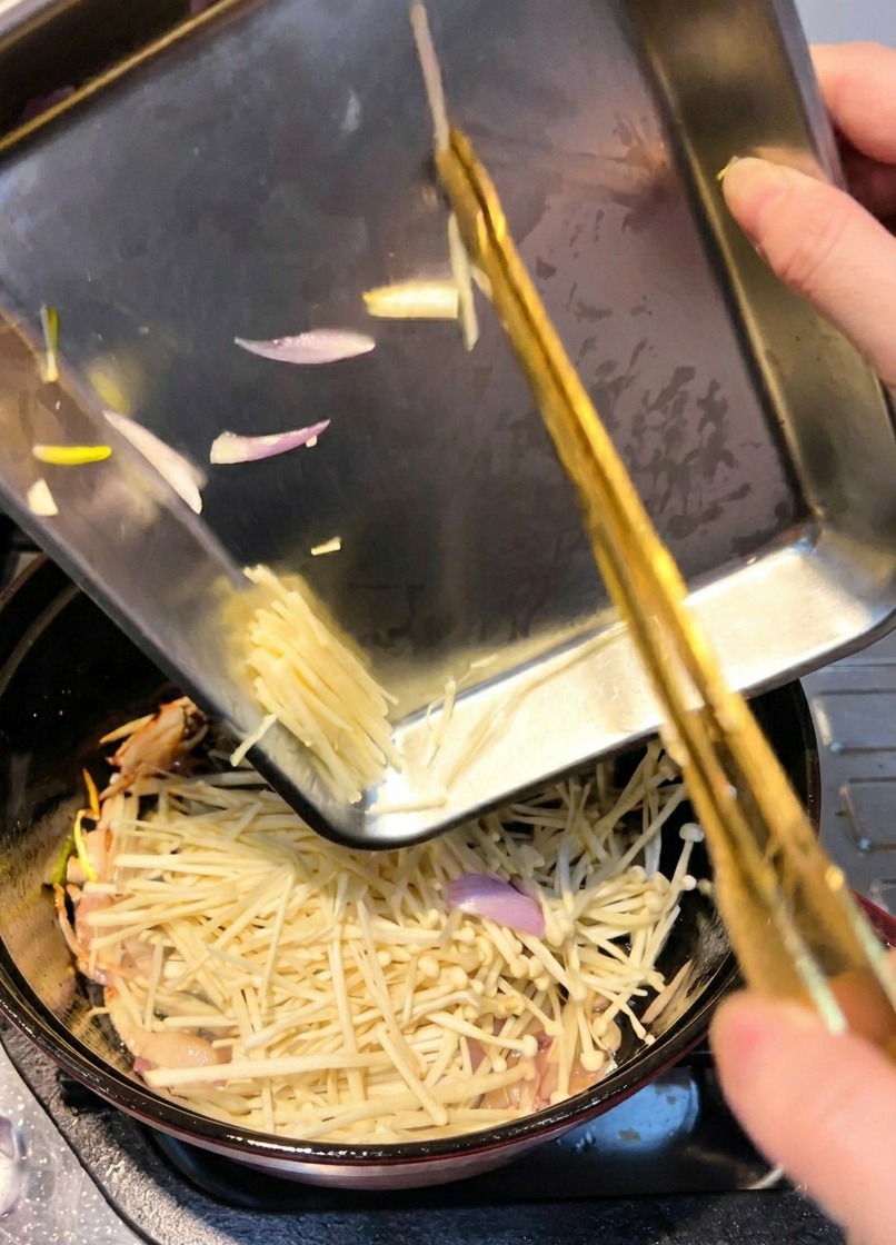 Champignons enoki ajoutés dans une cocotte pour être sautés avec des échalotes revenues.