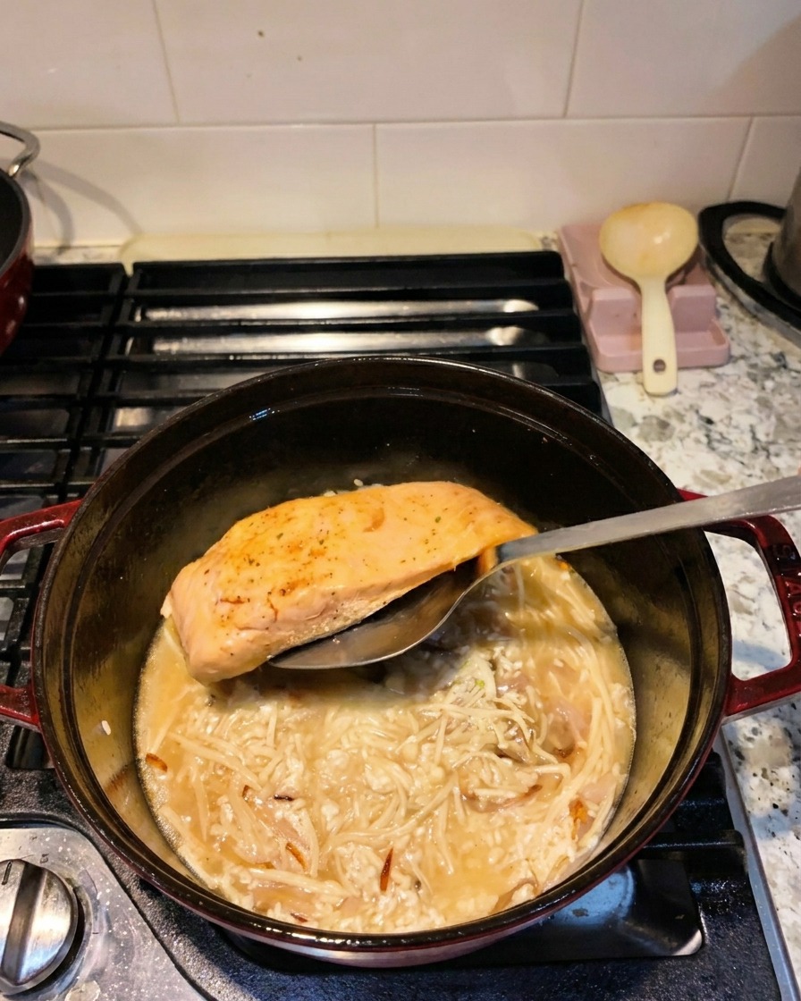 Une spatule déposant un filet de saumon saisi dans une cocotte contenant le riz et le liquide de cuisson.