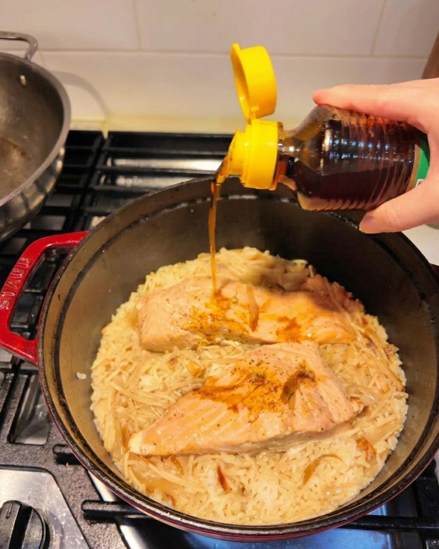 Huile de sésame grillé versée dune bouteille sur le plat de saumon et riz terminé.