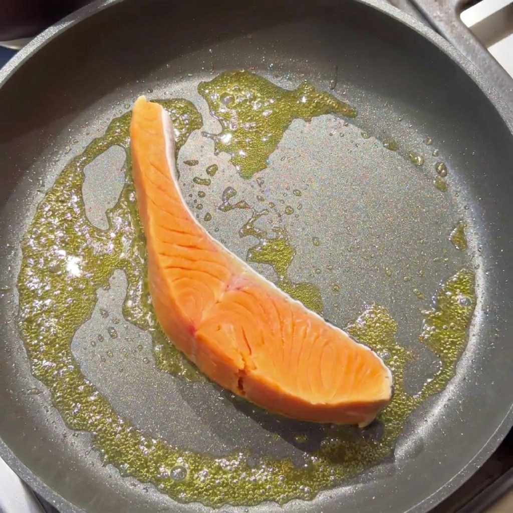 Un pavé de saumon cru saisissant dans une poêle avec du beurre moussant.