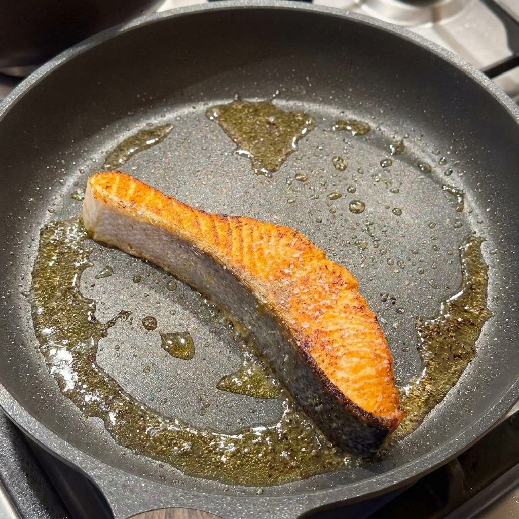 Pavé de saumon poêlé assaisonné de sel et de poivre noir dans la poêle.