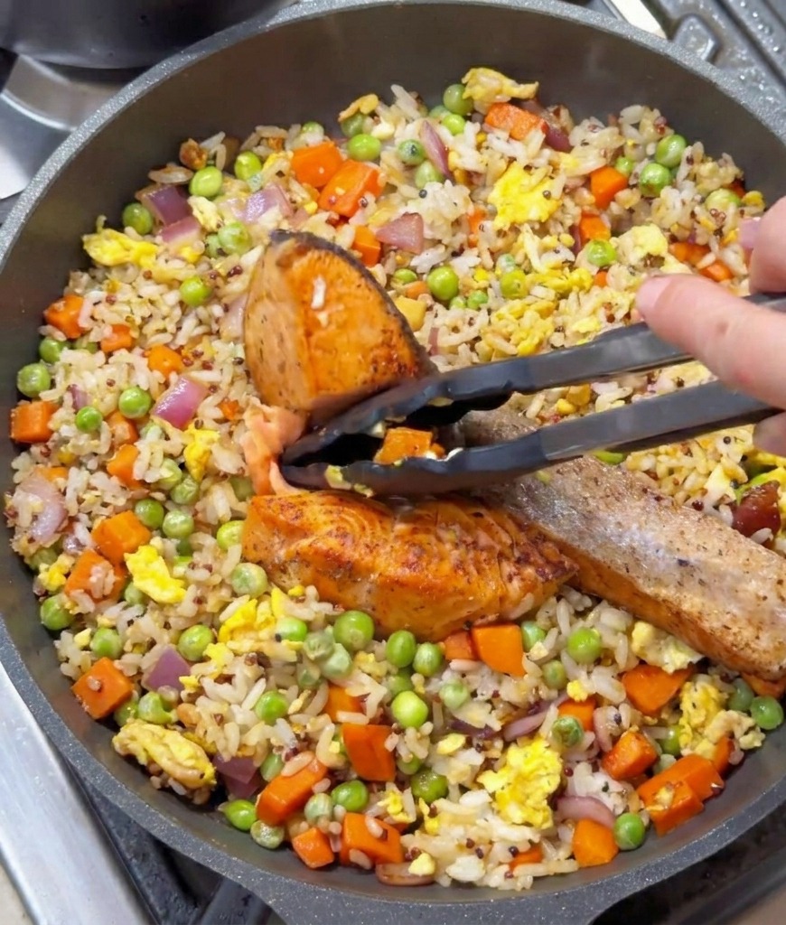 Pince de cuisine tenant un morceau de saumon poêlé au-dessus de la poêle de riz sauté.