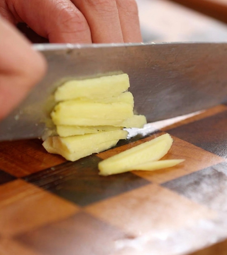 Gros plan dun couteau hachant finement une tranche de gingembre frais sur une planche en bois.