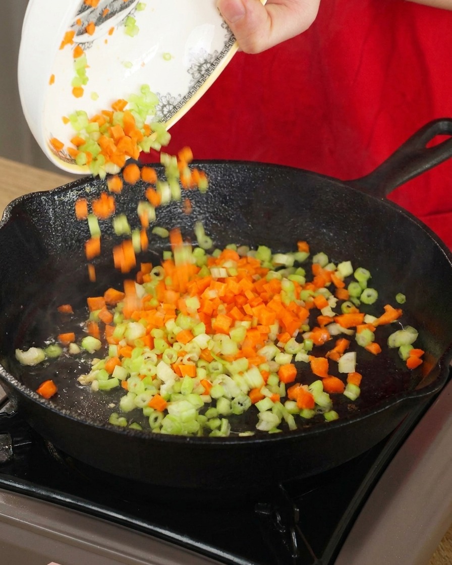 Dés de carottes et de céleri versés dun bol blanc dans une poêle en fonte chaude pour être sautés.
