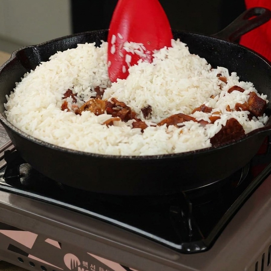 Riz et champignons remués avec une spatule rouge dans une poêle en fonte.